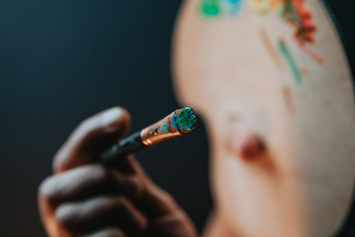 Hand holds a paint brush towards the camera