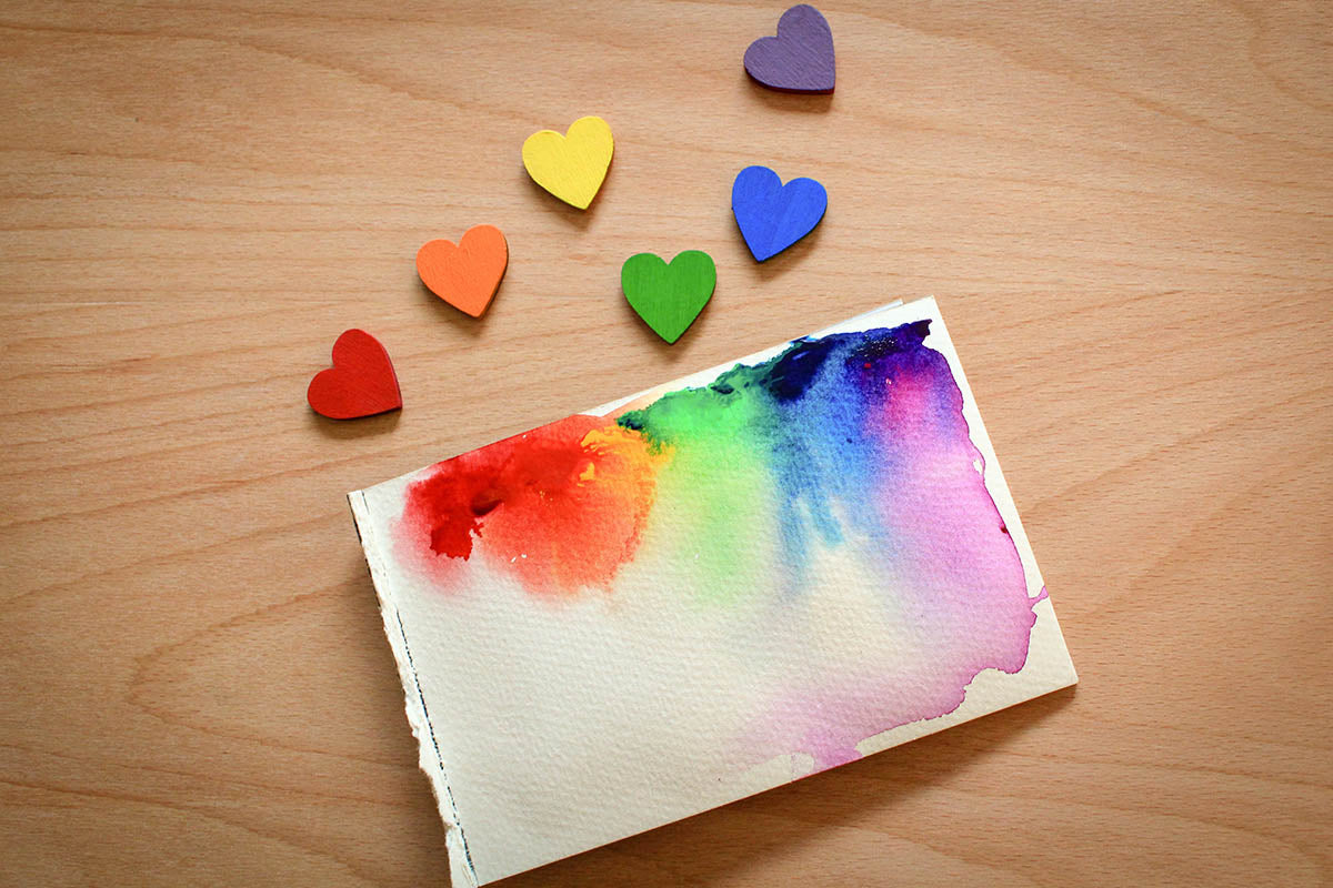 Rainbow painted wooden hearts beside watercolour canvas