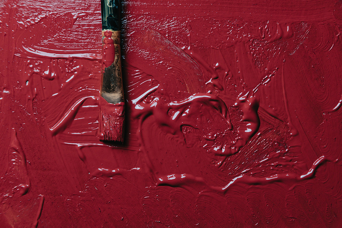 Wet red paint with a paint brush laying on it