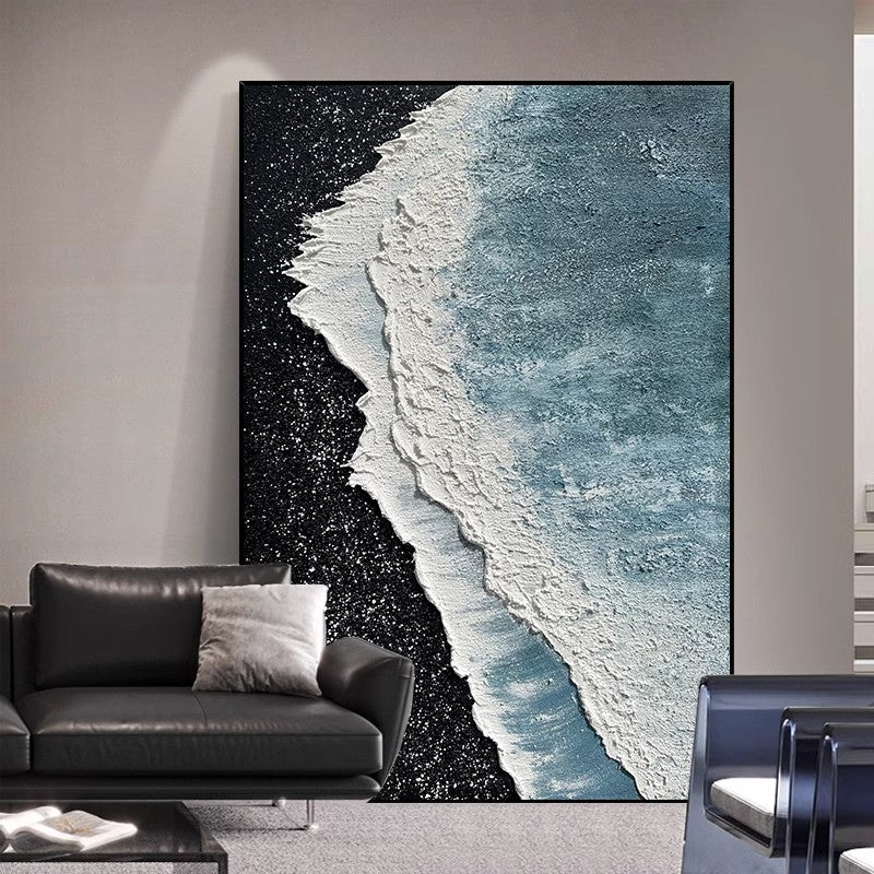 Black and white beach abstract painting against the wall behind the black sofa